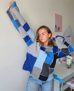 a woman standing in front of a white wall holding onto a blue and grey sweater