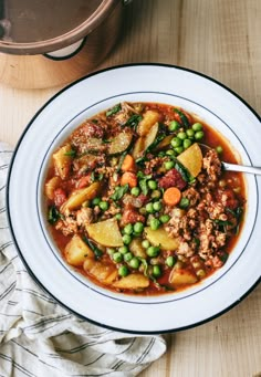 a bowl of stew with peas, carrots and meat on a table next to a pot