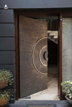 an open door with a circular design on the front and side panels, in between two potted plants