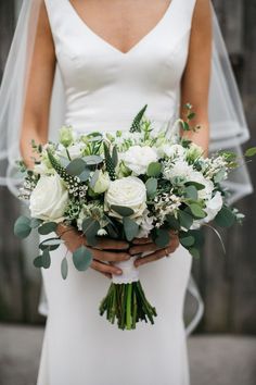 a bride holding a bouquet of white flowers and greenery