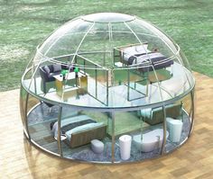 a glass dome house with couches and tables inside on a wooden floor in the middle of a grassy area