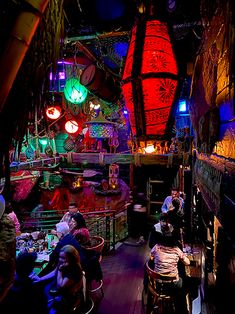 several people sitting at tables in a room with lights hanging from the ceiling and decorations on the walls