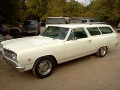 an old white station wagon is parked in a parking lot with other cars behind it