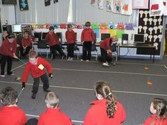 a group of children in red shirts are playing with sticks and balls on an indoor court