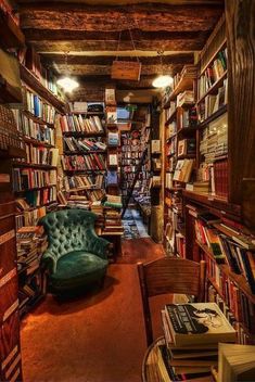 a room filled with lots of books next to a green chair and wooden shelves full of books