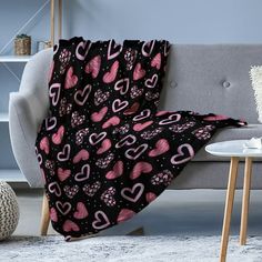 a black couch with pink hearts on it next to a white coffee table and lamp