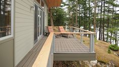 a deck with two chairs on it next to a house and trees in the background