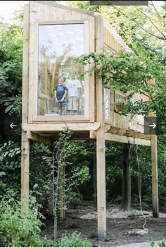 two people standing in the window of a tree house that is surrounded by greenery