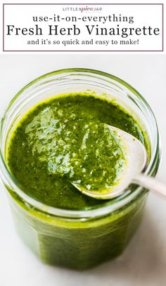 a spoon in a jar filled with green pesto on top of a white table