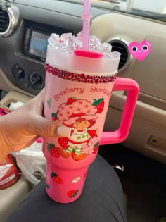 someone holding up a pink cup with strawberries on it in the backseat of a car