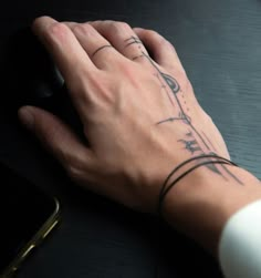 a person's hand with a tattoo on their wrist holding a computer mouse next to a cell phone