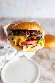 a hamburger with cheese, tomato and lettuce is held up in front of a plate