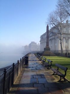 a row of benches sitting on top of a sidewalk next to a park covered in fog