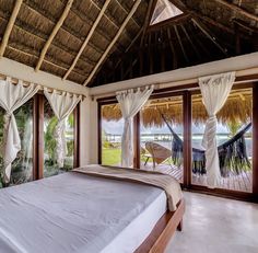 a large bed sitting under a window next to a wooden ceiling covered in white curtains