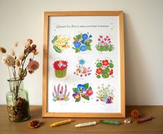 a vase filled with flowers sitting next to a framed artwork on top of a wooden table