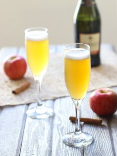 two wine glasses filled with apple cider on a table next to an apple and cinnamon stick