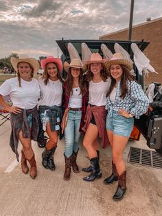 four girls in cowboy hats standing next to a truck on the side of the road