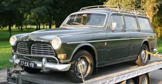 an old car is on the back of a flatbed tow truck in a park