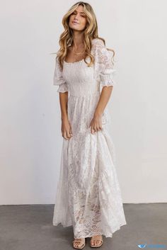 a woman wearing a white dress and sandals standing in front of a wall with her eyes closed