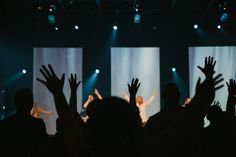 silhouettes of people on stage with their hands up in the air