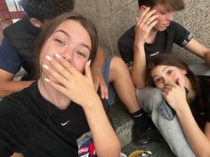 three young people sitting on the ground with their hands in their mouths and looking at the camera