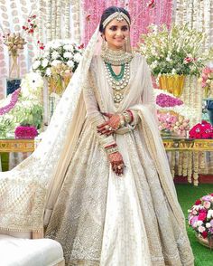 a woman in a white and gold bridal gown posing for the camera with flowers behind her