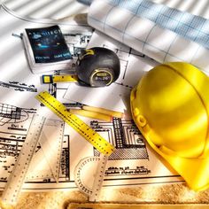 a hard hat, measuring tape and other construction equipment on top of blueprints