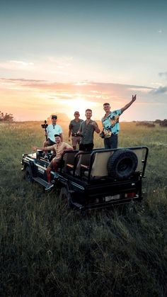 four men standing on the back of a truck in a field with their arms up