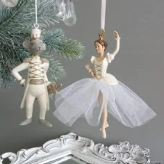 two ornaments hanging from a christmas tree in the shape of mice, one wearing a tutu and holding a nutcracker