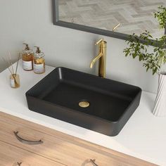 a black sink sitting on top of a white counter next to a mirror and potted plant