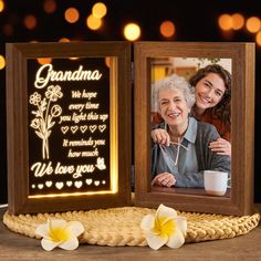 an illuminated photo frame with the words grandma on it and two white flowers next to it