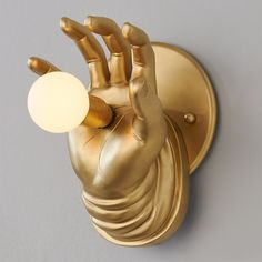 a gold hand light on a wall with a white ball in the middle and two fingers out