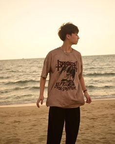 a young man standing on top of a sandy beach next to the ocean at sunset