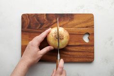 a person cutting onions with a knife on a wooden cutting board next to a white wall