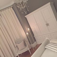 a white bed sitting in a bedroom next to a dresser and chair with a chandelier hanging from the ceiling