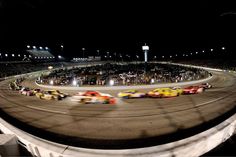 a group of cars driving around a track at night