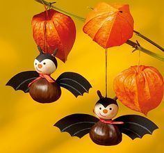 two halloween decorations hanging from a branch with orange leaves and pumpkins in the background