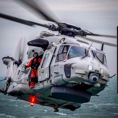 a helicopter flying over the ocean with a man standing on it's front end