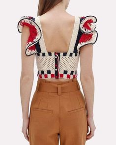 the back of a woman wearing brown pants and a white top with red, black, and blue designs on it