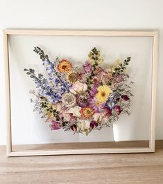 an arrangement of flowers is displayed in a wooden frame on a shelf next to a wall