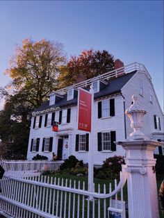 a large white house with a red sign on it's front gate and trees in the background