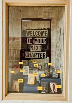 a window display with books and other items in the front, including a welcome to your next chapter sign