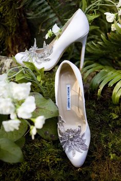 two white shoes sitting on top of a moss covered ground next to flowers and plants