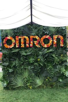 a sign that says omron surrounded by plants and flowers in front of a white tent