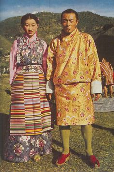 two people standing next to each other in front of a hill with trees and grass