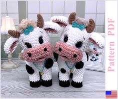 two crocheted cow stuffed animals sitting next to each other on top of a table