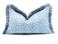 a blue and white leopard print pillow with tassels on the bottom, sitting on a white surface