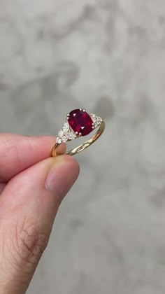 a person holding up a ring with a red stone in the middle and white diamonds around it