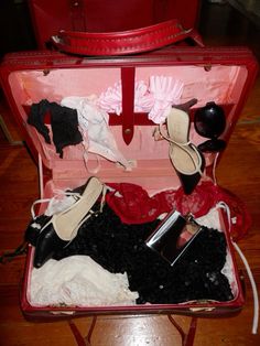 an open suitcase filled with clothes and shoes on top of a wooden floor next to a red bag