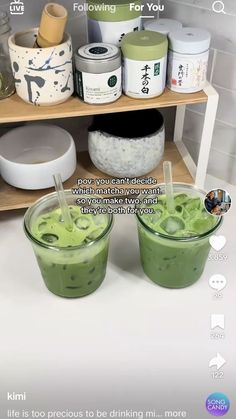 two glasses filled with green liquid sitting on top of a counter next to bowls and containers